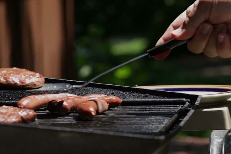 someone cooking hot dogs on the grill