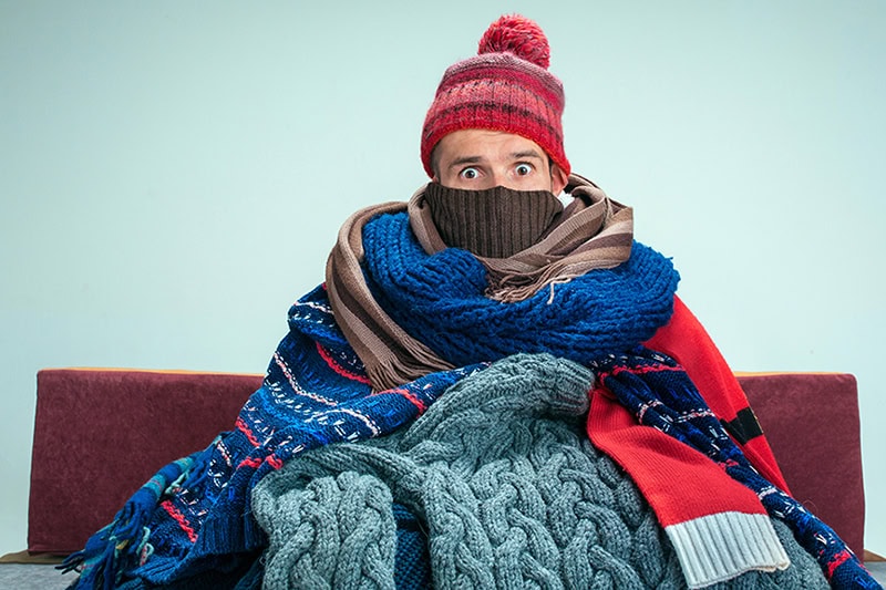 Winterizing Your HVAC Equipment: Cozy Tips From Stout Heating & Air Conditioning, Inc. A woman sitting on her couch bundled in blankets.